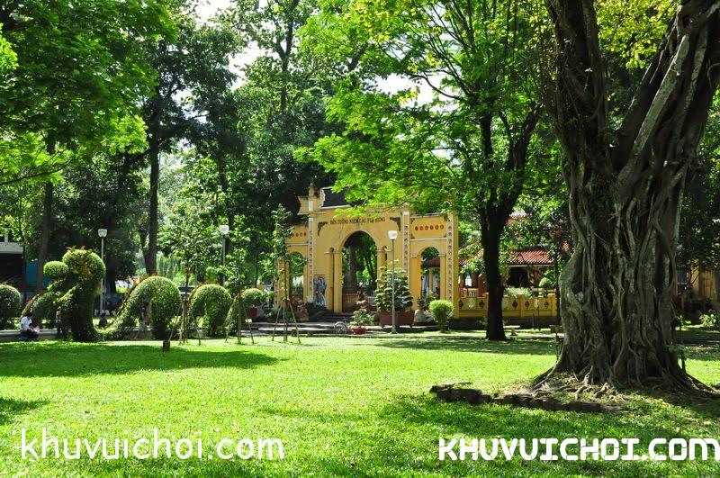 Công Viên Tao Đàn 1 Cổng kiến trúc màu vàng giữa thảm cỏ và cây cổ thụ trong công viên râm mát