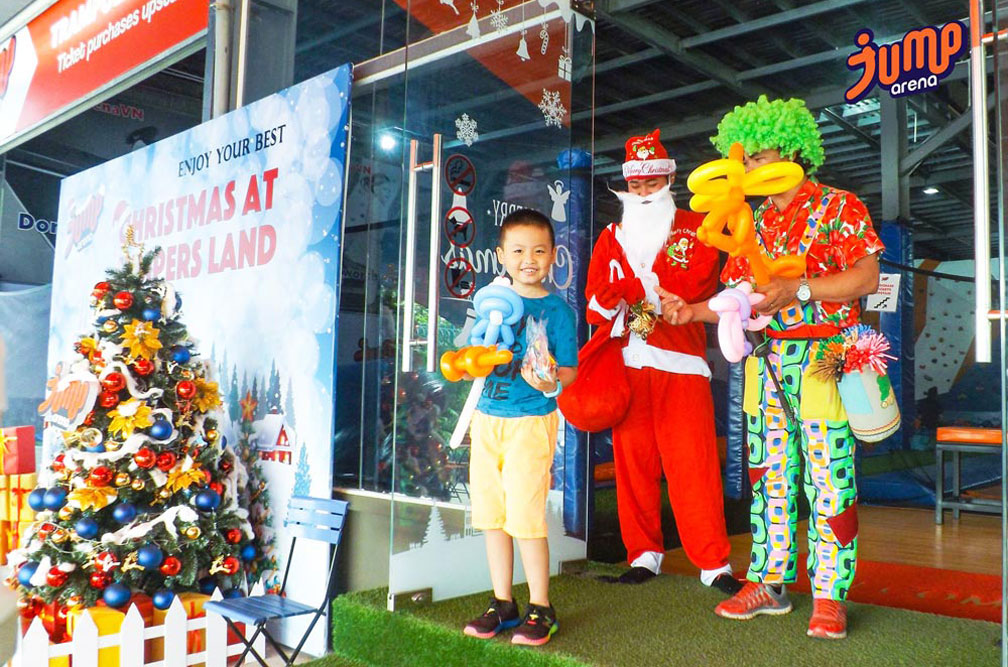 Cậu bé cầm bong bóng đứng cùng ông già Noel và chú hề bên cây thông
